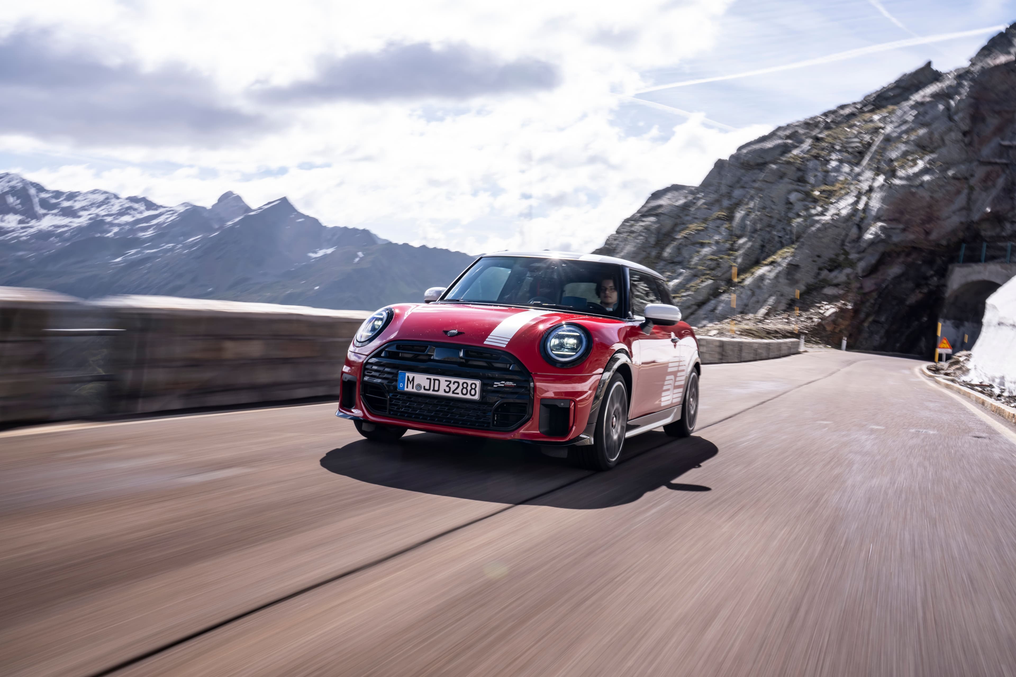 MINI 1965 Victory Edition rojo con techo blanco circulando por una carretera de montaña.